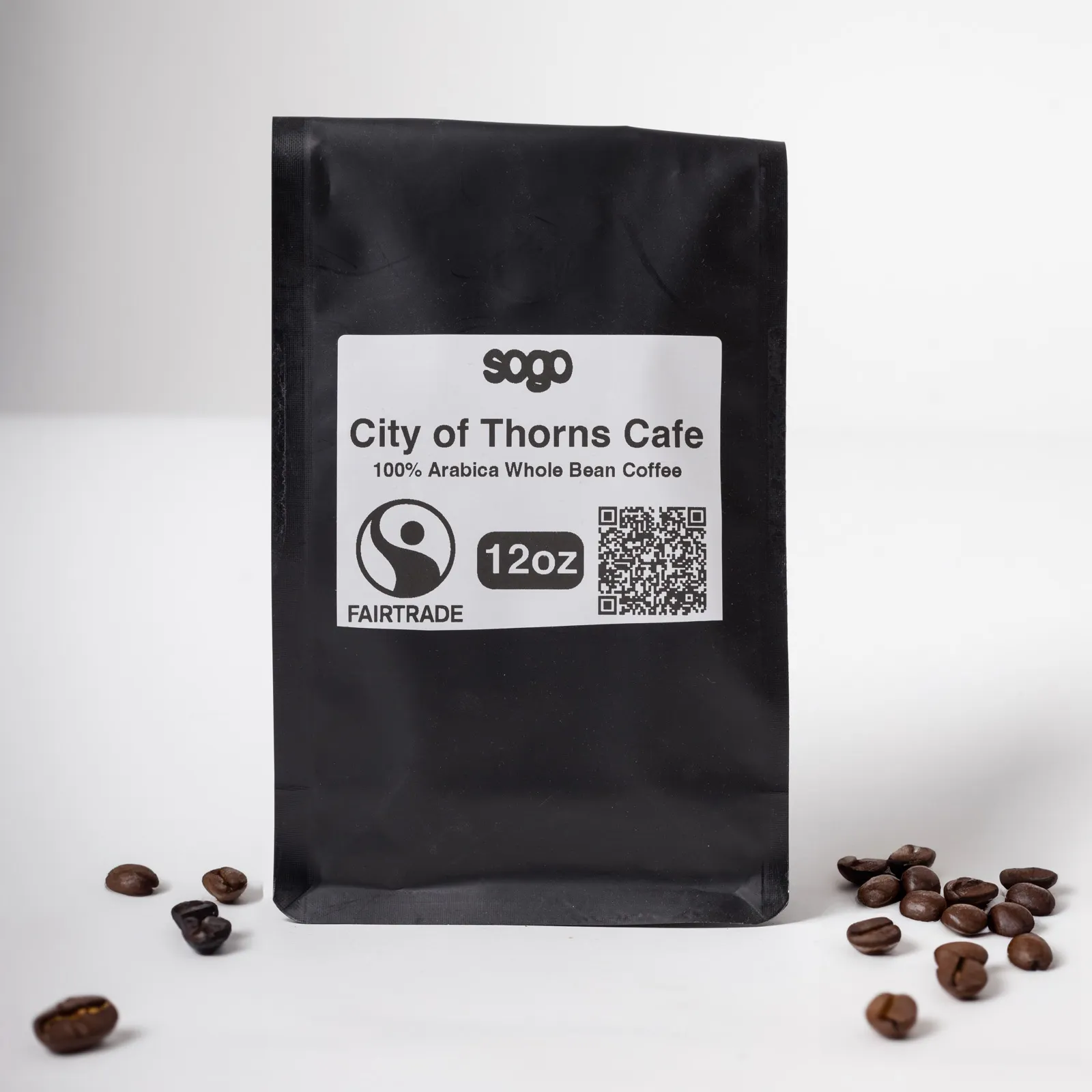 A black 12 oz bag of City of Thorns Cafe whole bean coffee, beside scattered roasted beans.