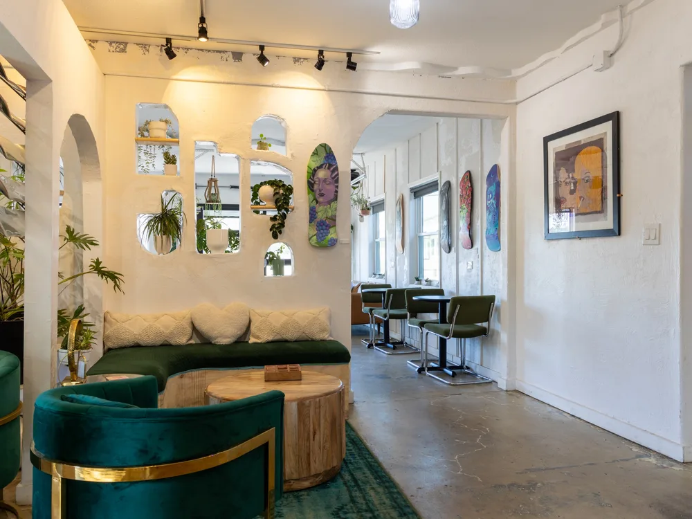 The lounge: green velvet seating and a round wood table against the hand-sculpted plaster niche wall, plants in every cut-out