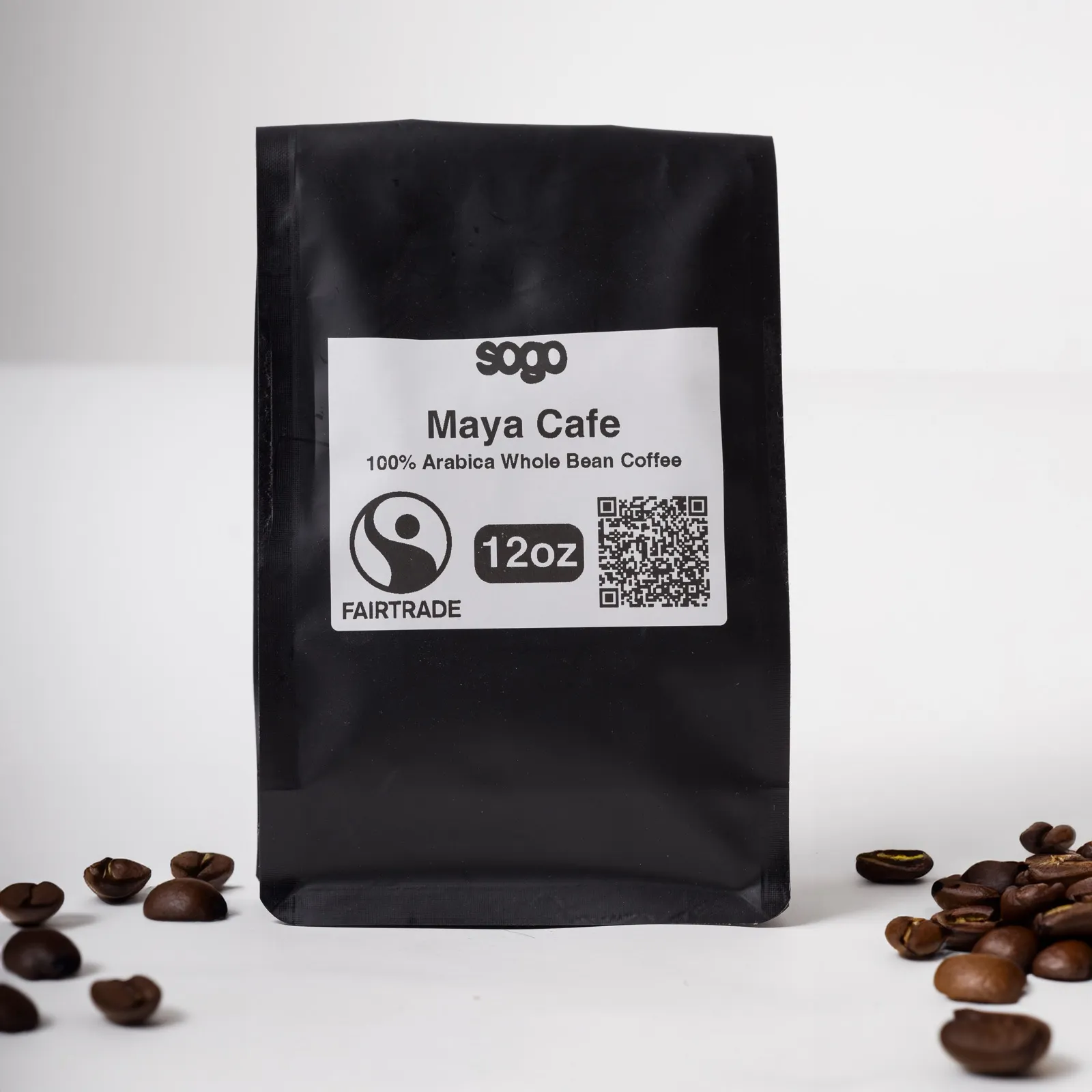 A black 12 oz bag of Maya Cafe whole bean coffee, beside scattered roasted beans.