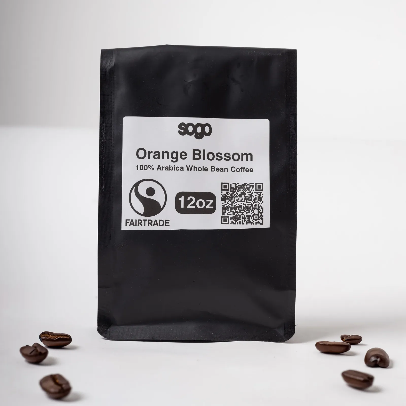 A black 12 oz bag of Orange Blossom whole bean coffee, beside scattered roasted beans.